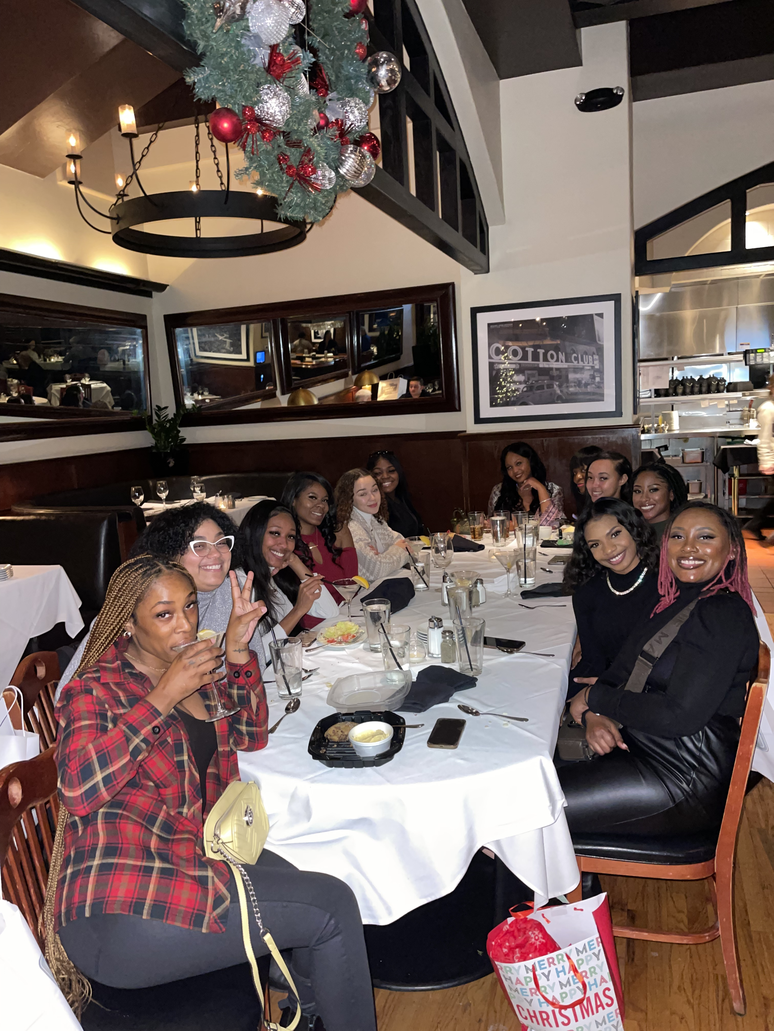 Pink Caviar group of women gathered around a table in a restaurant decorated for Christmas, with a Christmas wreath hanging above.