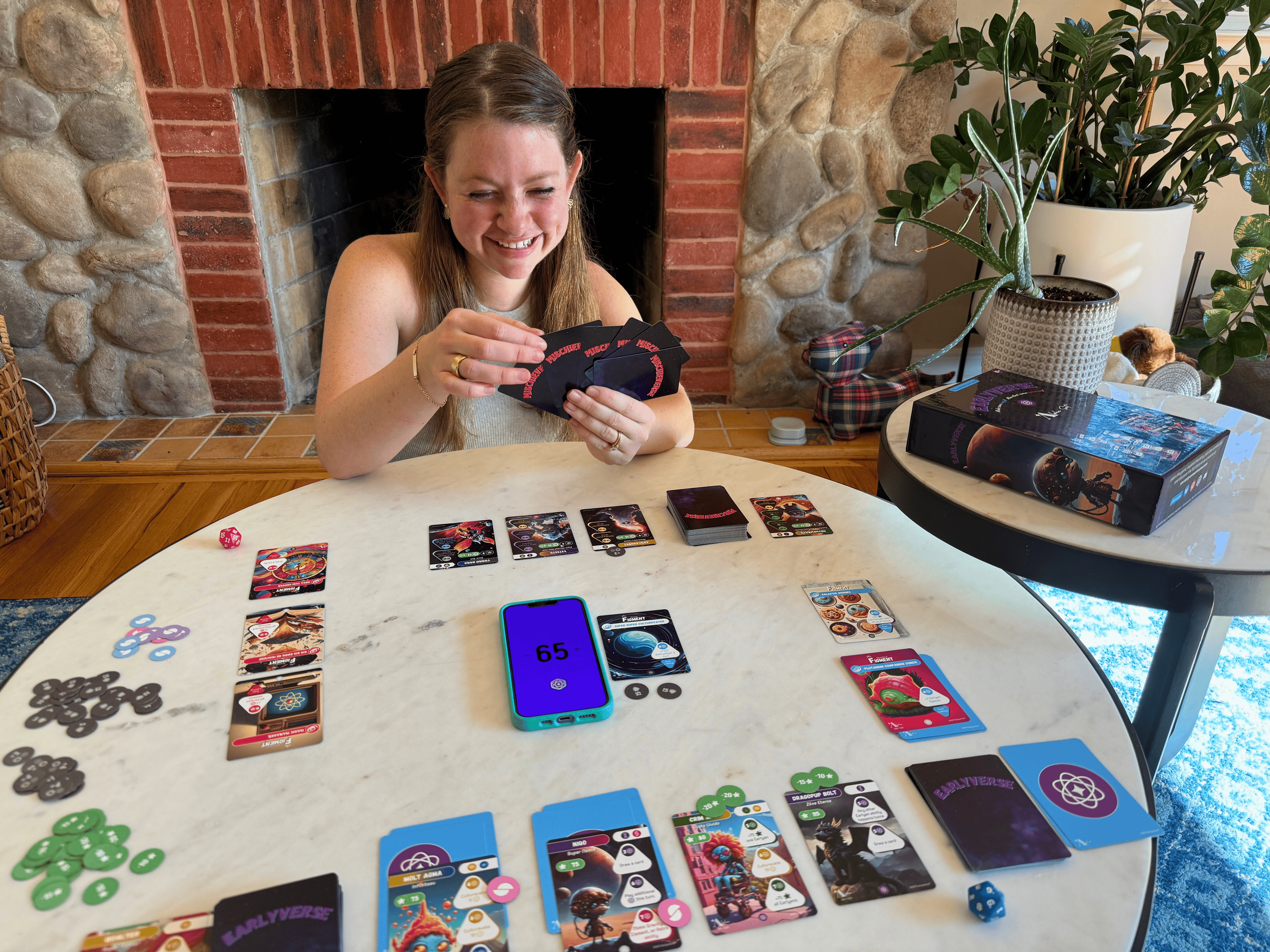 Woman smiling while choosing a Mischievent card from her hand, playing Earlyverse on a living room table.