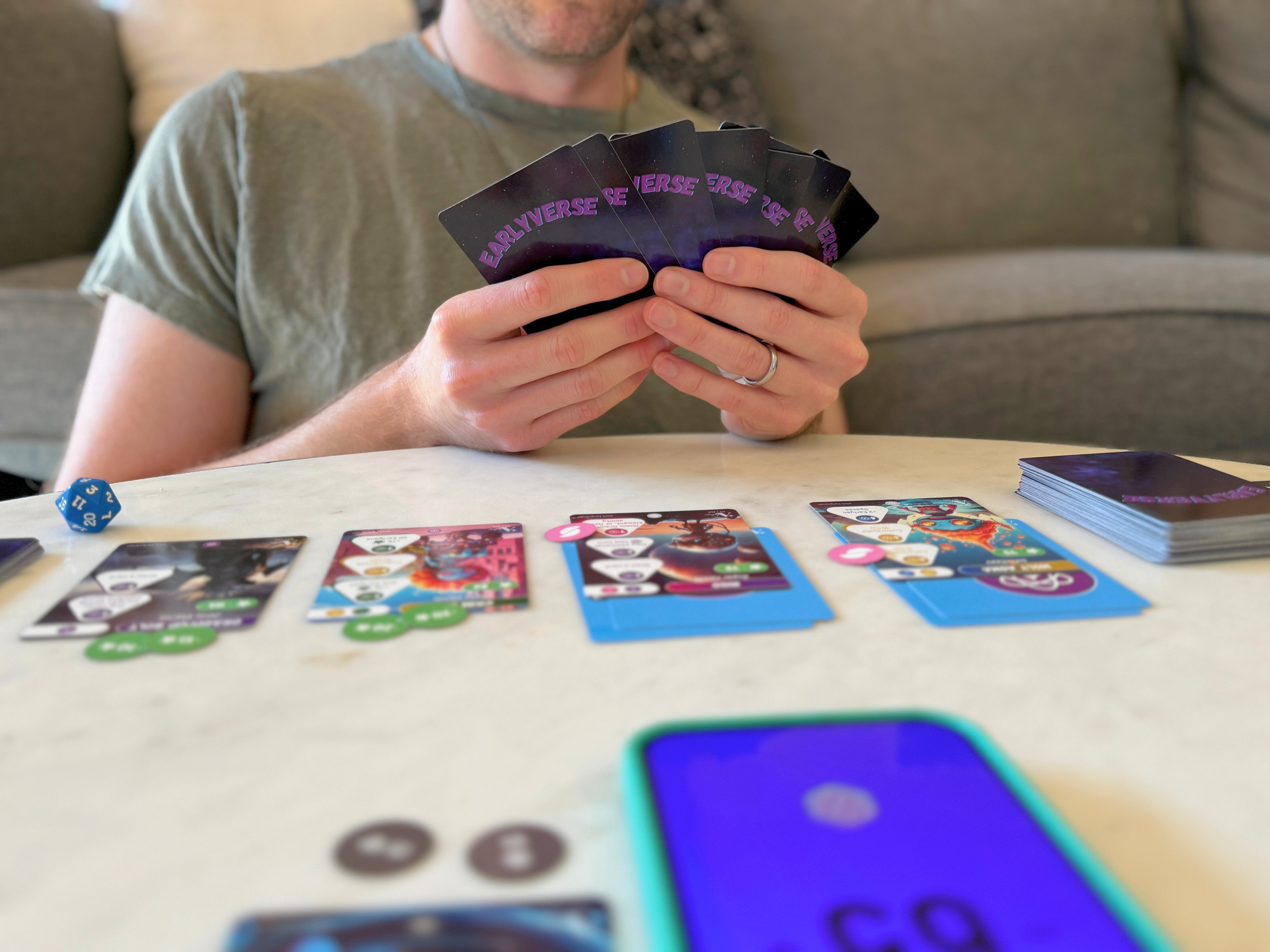 Man holding a hand of Earlyverse cards, playing Earlyverse at a living room table.
