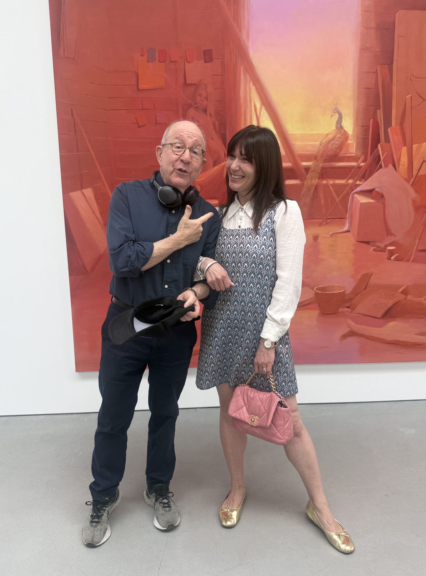 a man and a woman smiling in front of a red tone painting in a gallery