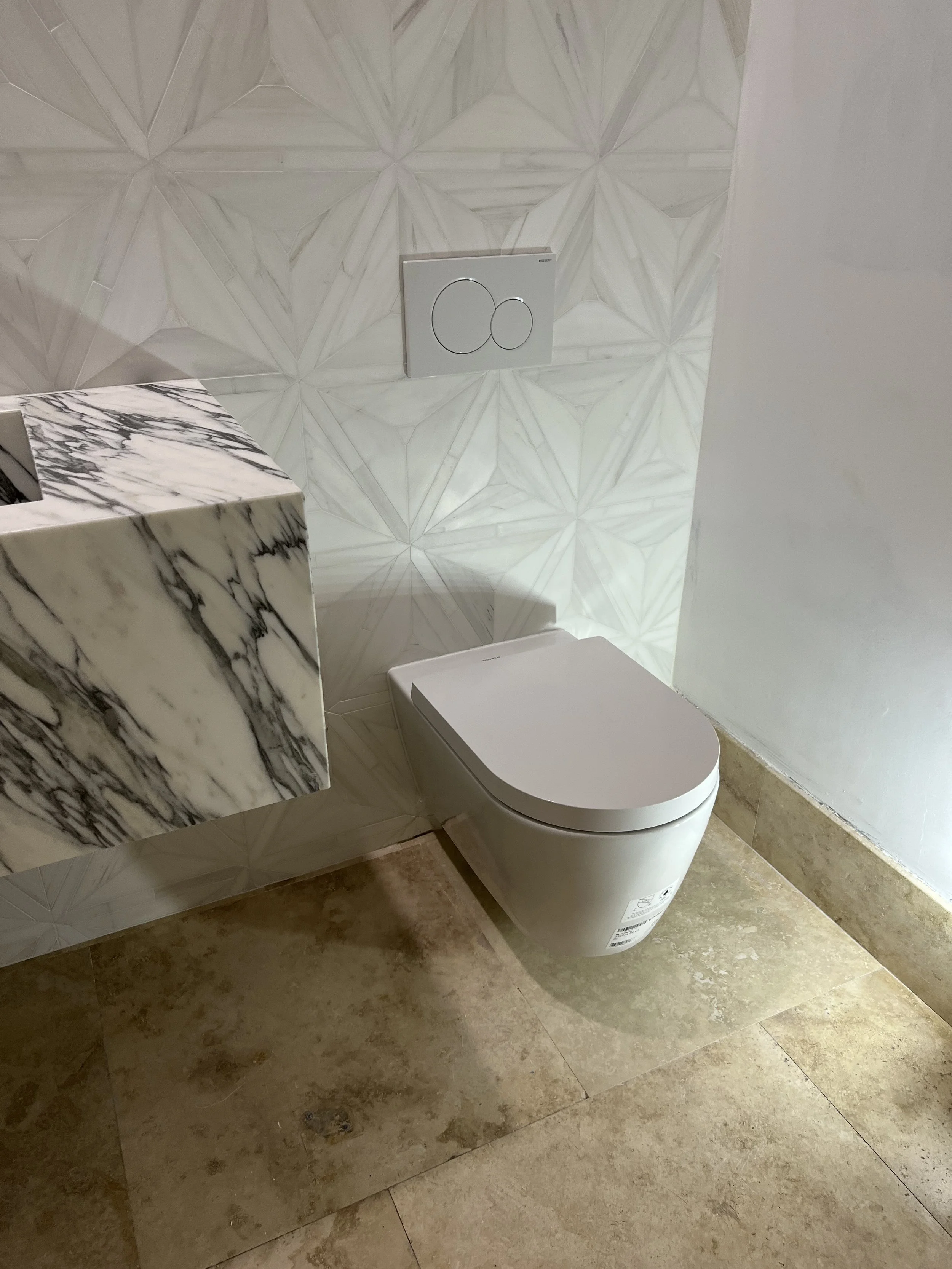 Modern bathroom with a wall-mounted toilet, geometric wall tiles, and a marble countertop.