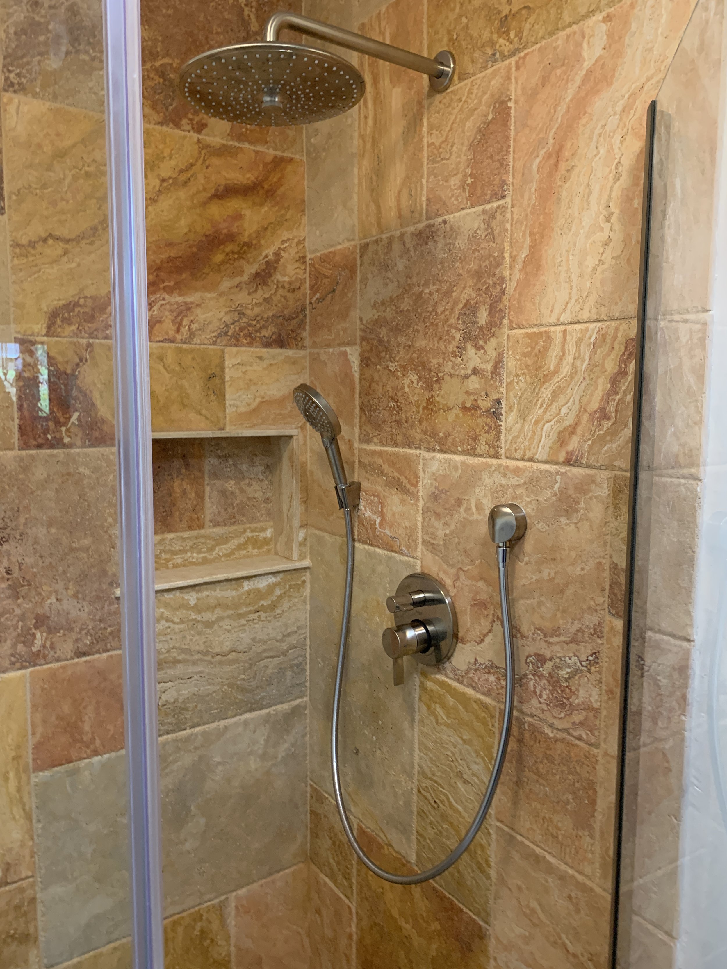 Modern shower with rainfall showerhead and detachable handheld sprayer, beige and brown stone tiles.