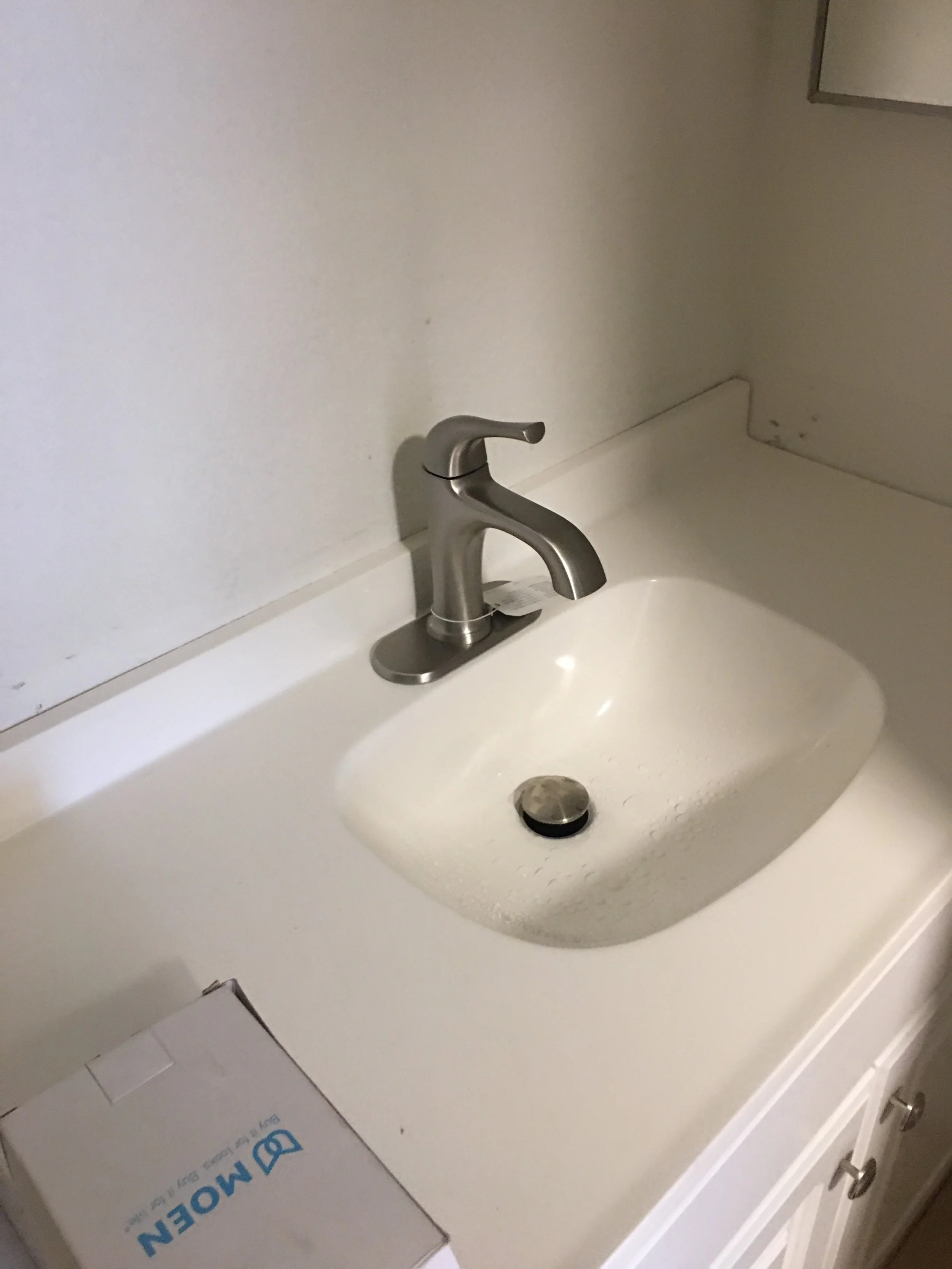 Bathroom sink with stainless steel faucet and a box labeled "Moen" on the counter.