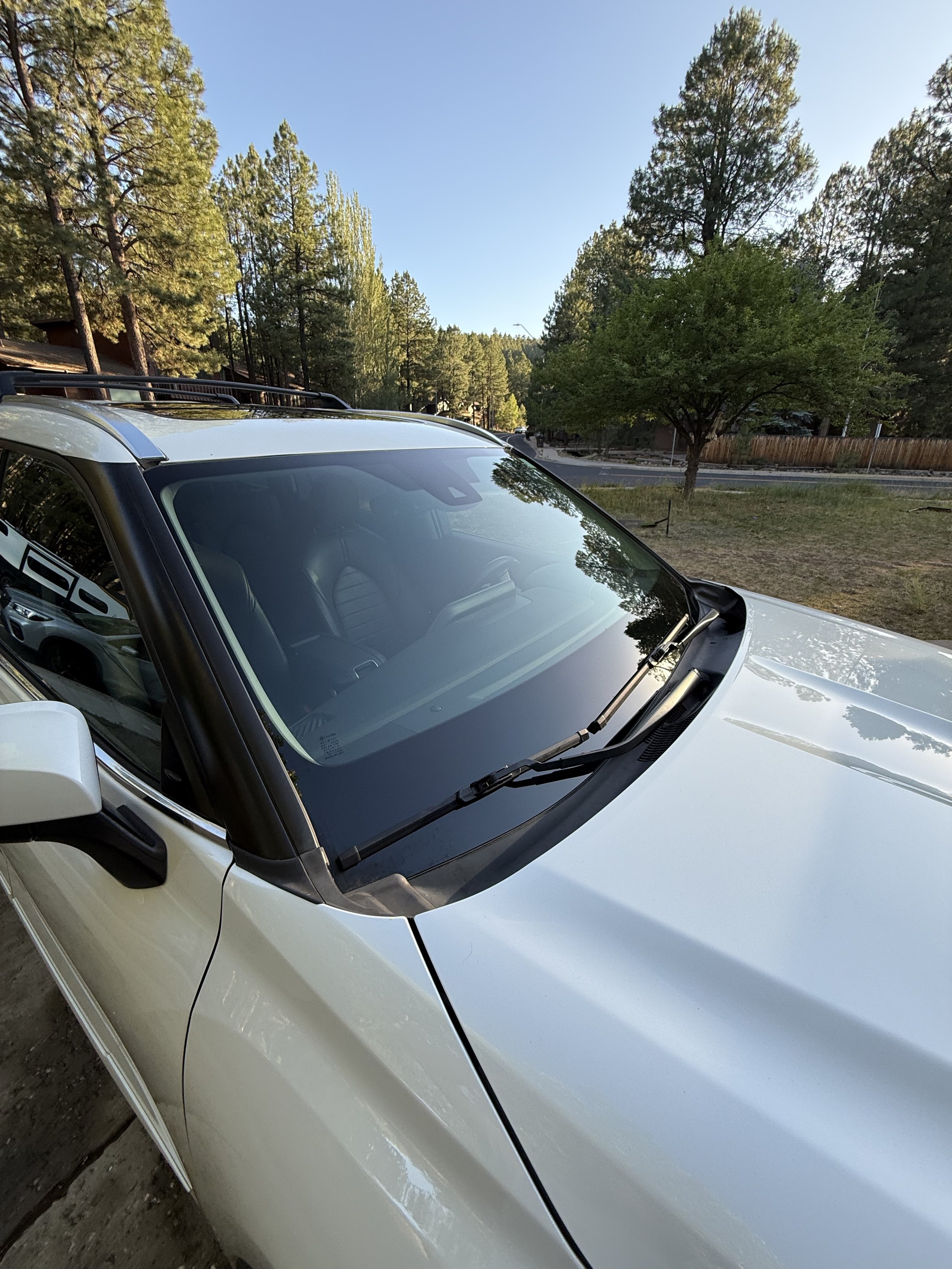 A white vehicle parked on a dirt surface, with trees and a street in the background under a clear sky.