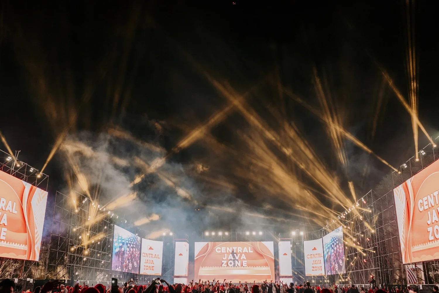 Music festival stage with bright lights, large screens displaying "Central Java Zone," and a crowd of people attending at night.