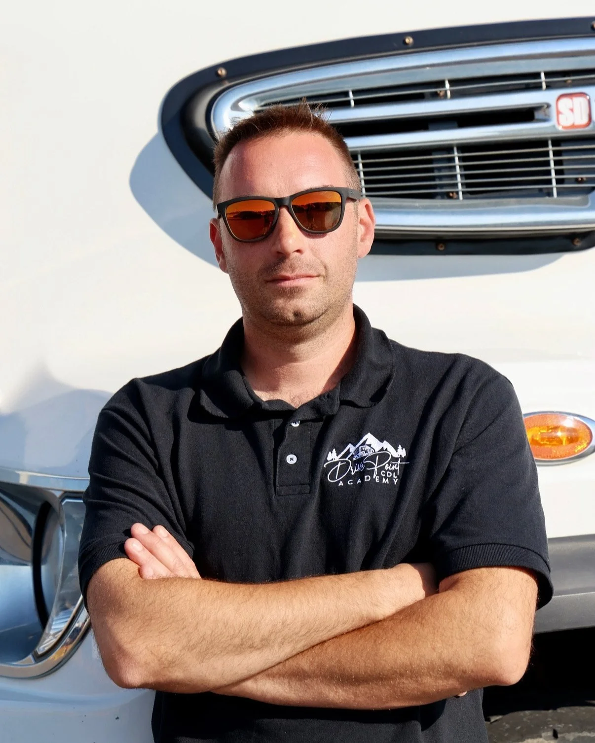 Person wearing sunglasses standing next to a large white truck labeled "Student Driver."