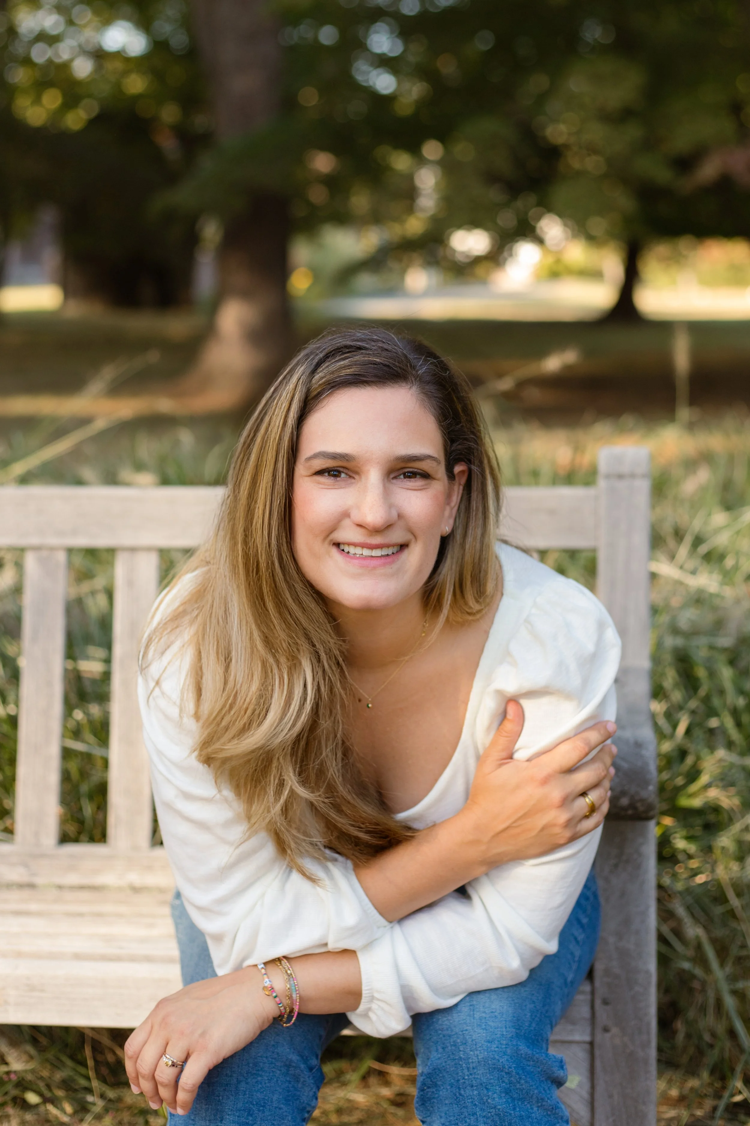 Person sitting on a blanket outdoors, wearing a tan sweatshirt and camouflage pants, with sunglasses on their head.