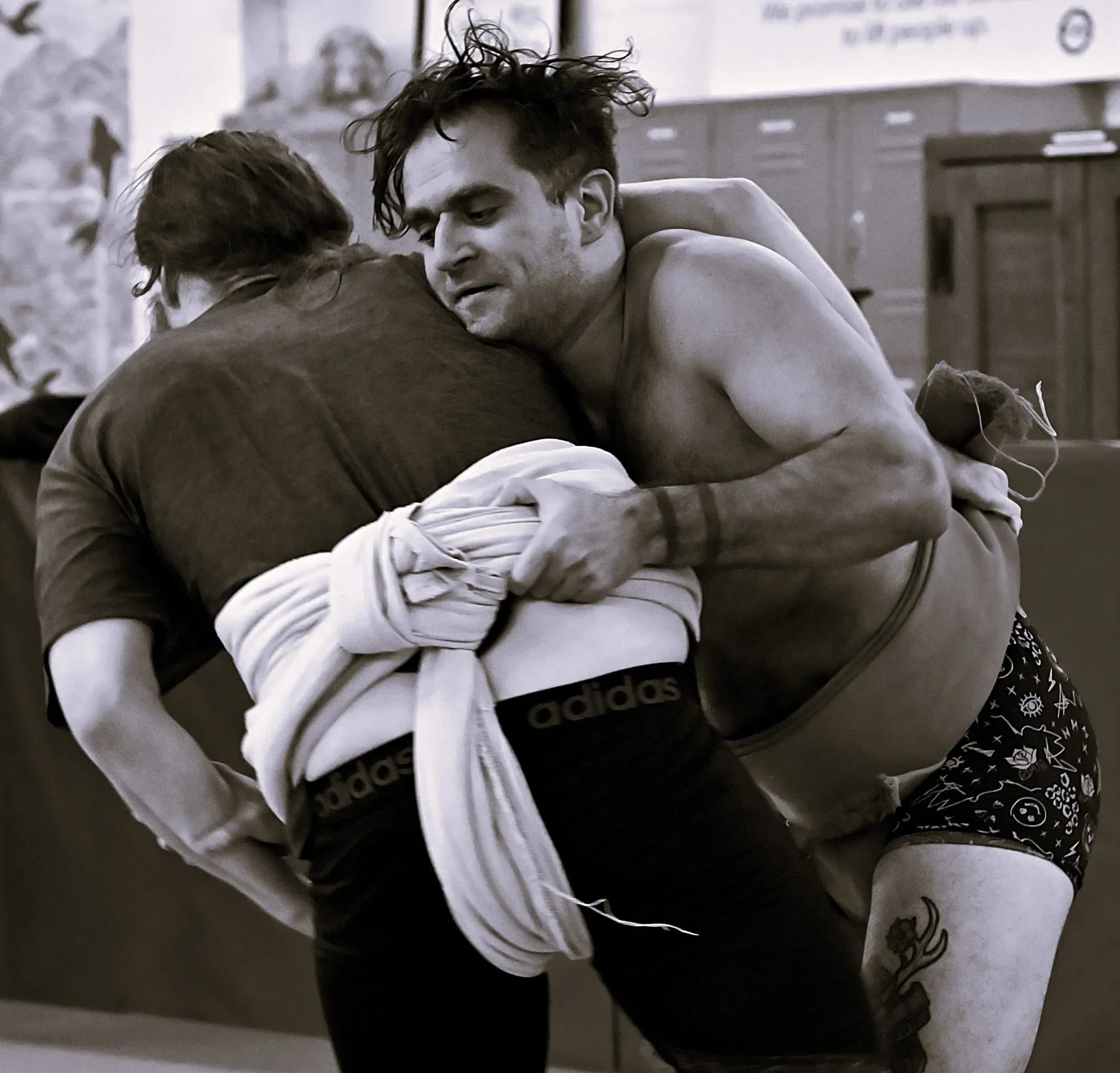 Two individuals wrestling on the floor in a gym or wrestling mat area.