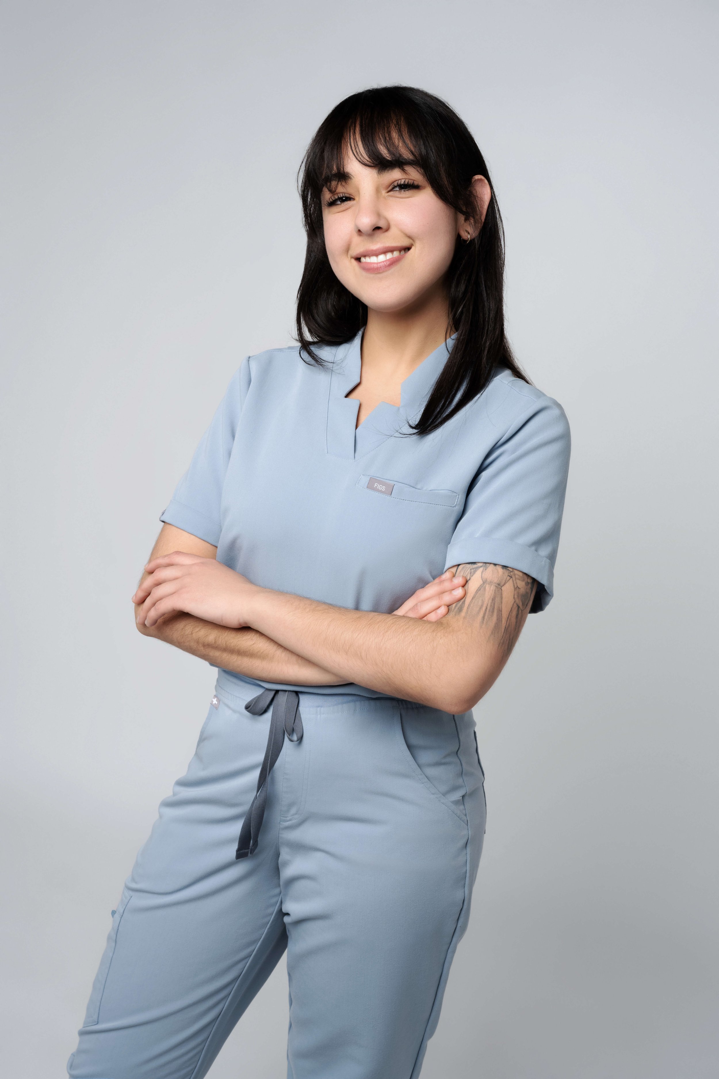 Smiling person in light blue scrubs with arms crossed.