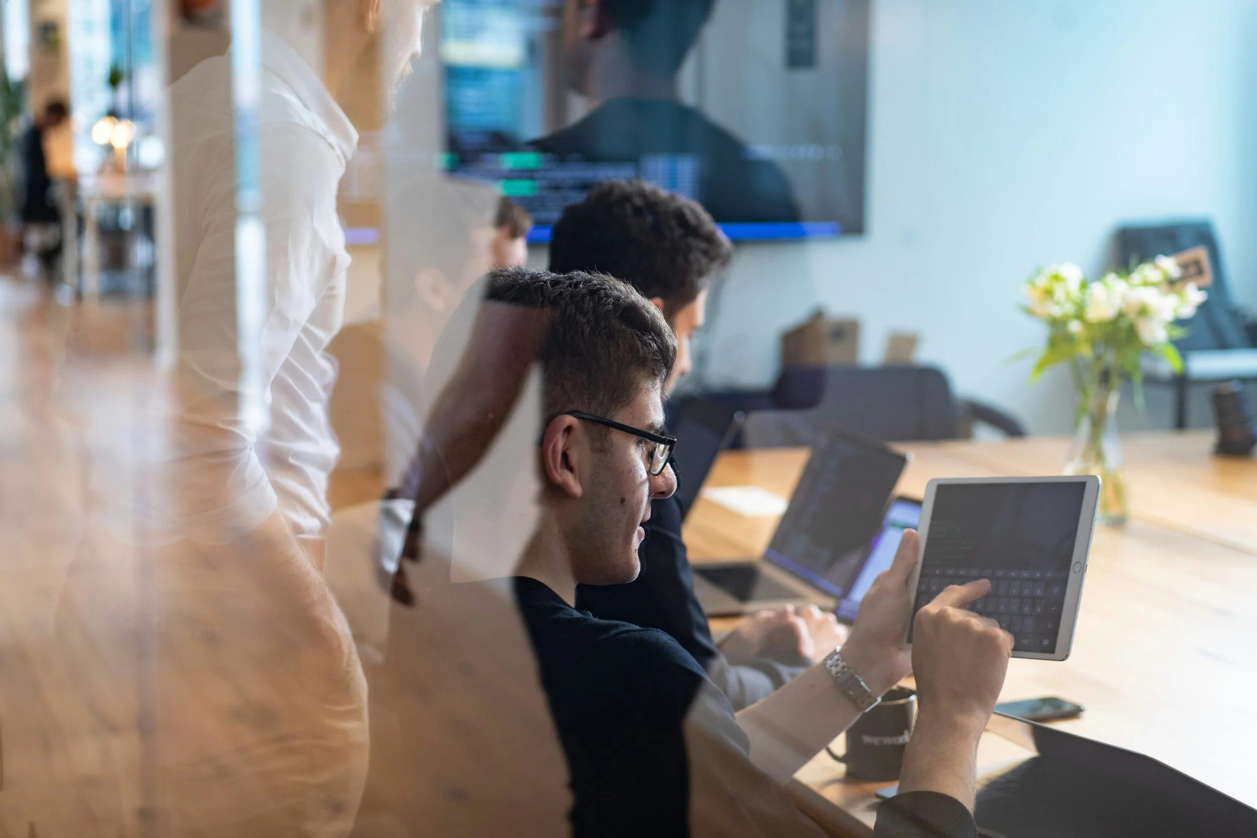 Group of people working on laptops and tablets around a conference table in an office.