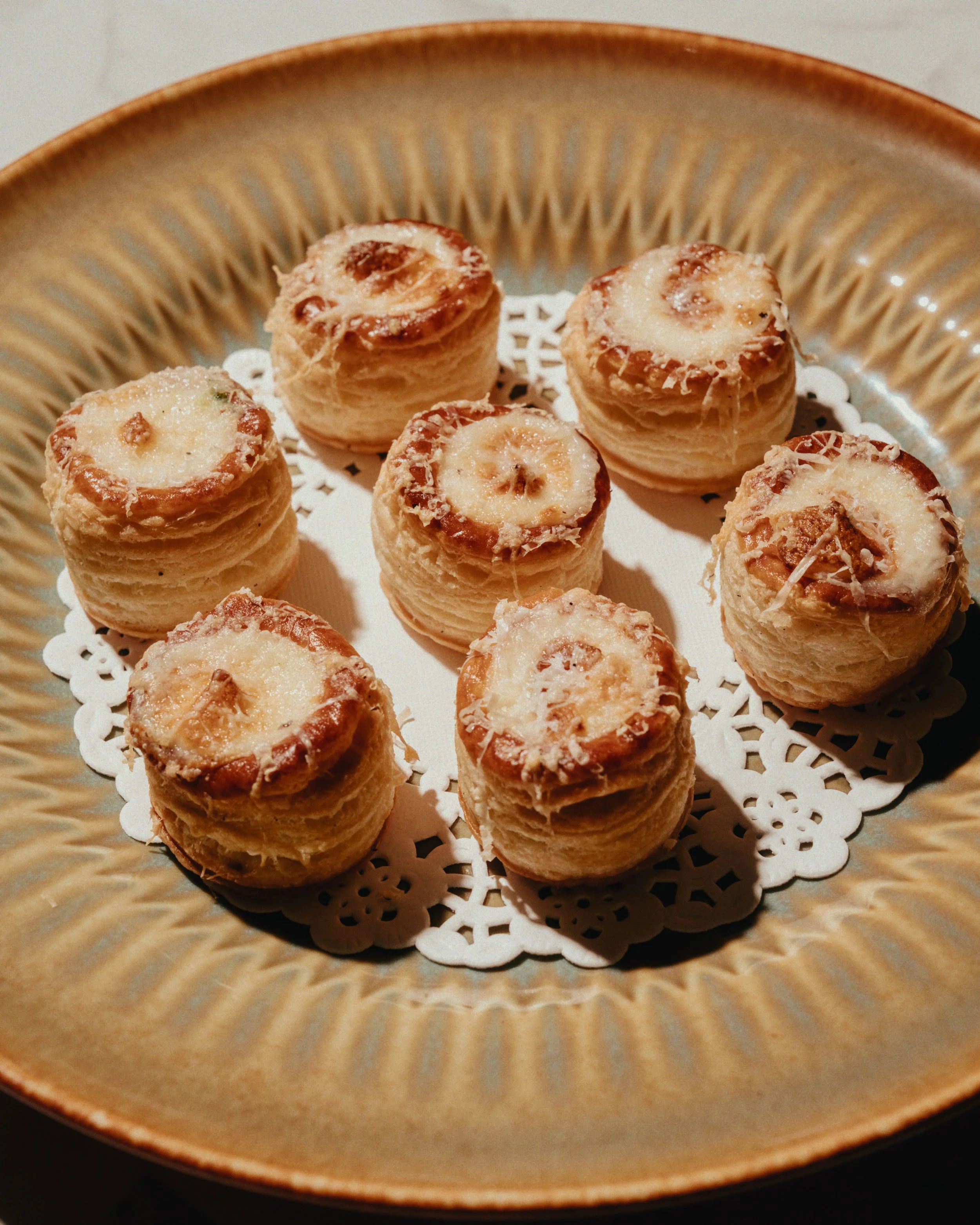 A ceramic plate with eight small banana cream pies on a paper doily.