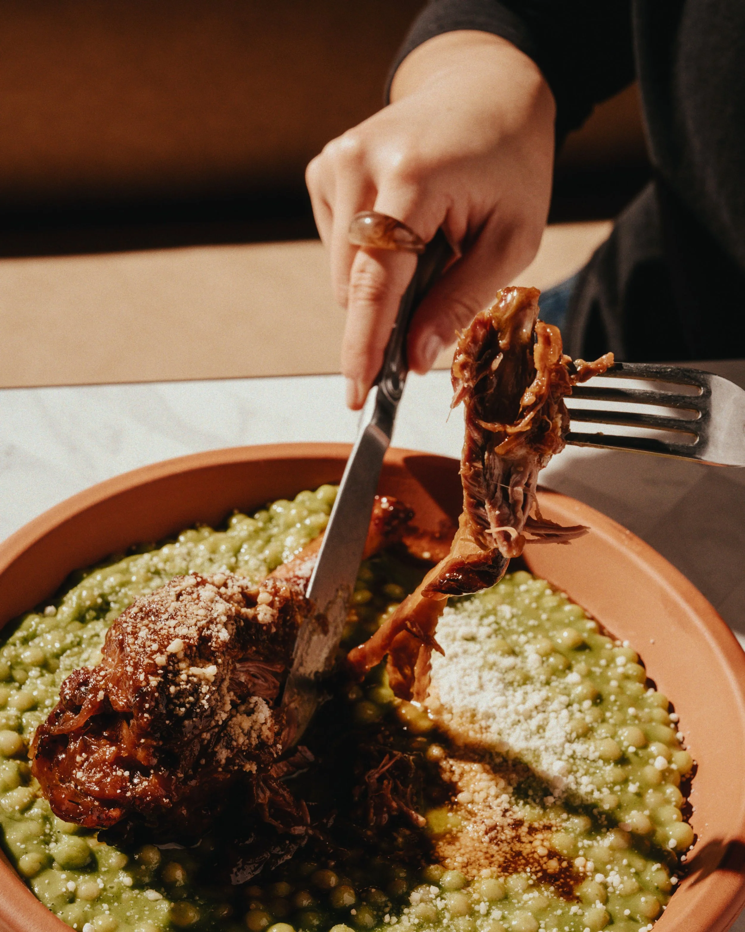 Person serving cooked meat onto a plate of green beans, with grated cheese on top.