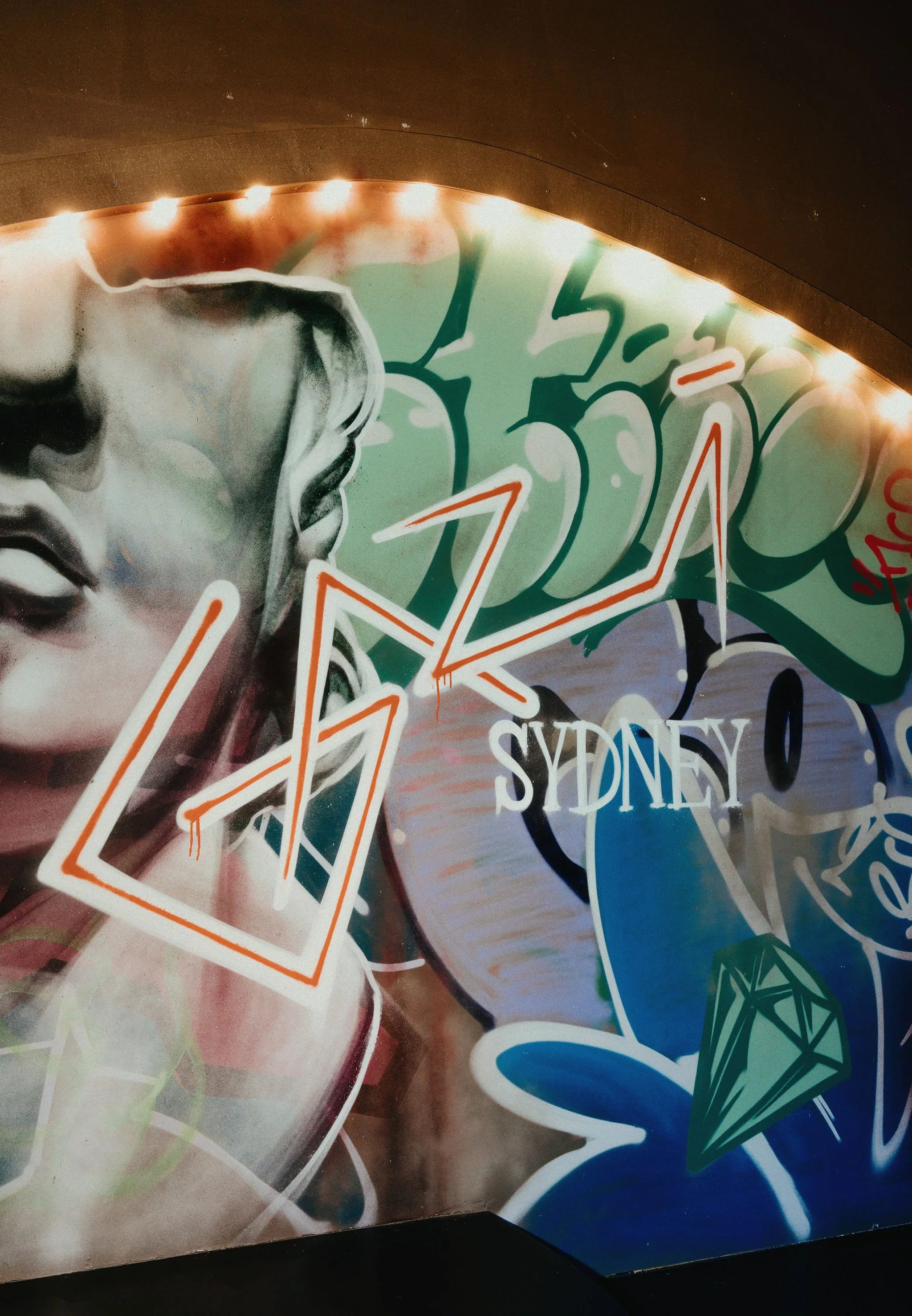 Graffiti art featuring a woman's face, the word 'Sydney,' a diamond, and various colorful abstract designs.