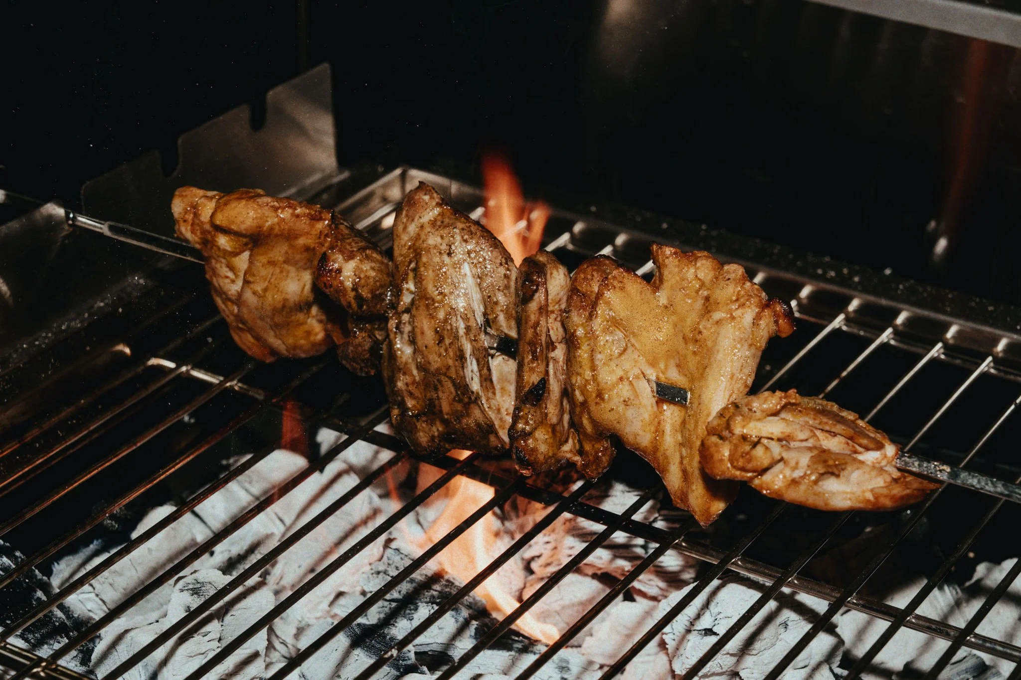 Meat skewers on a grill over charcoal and open flame.