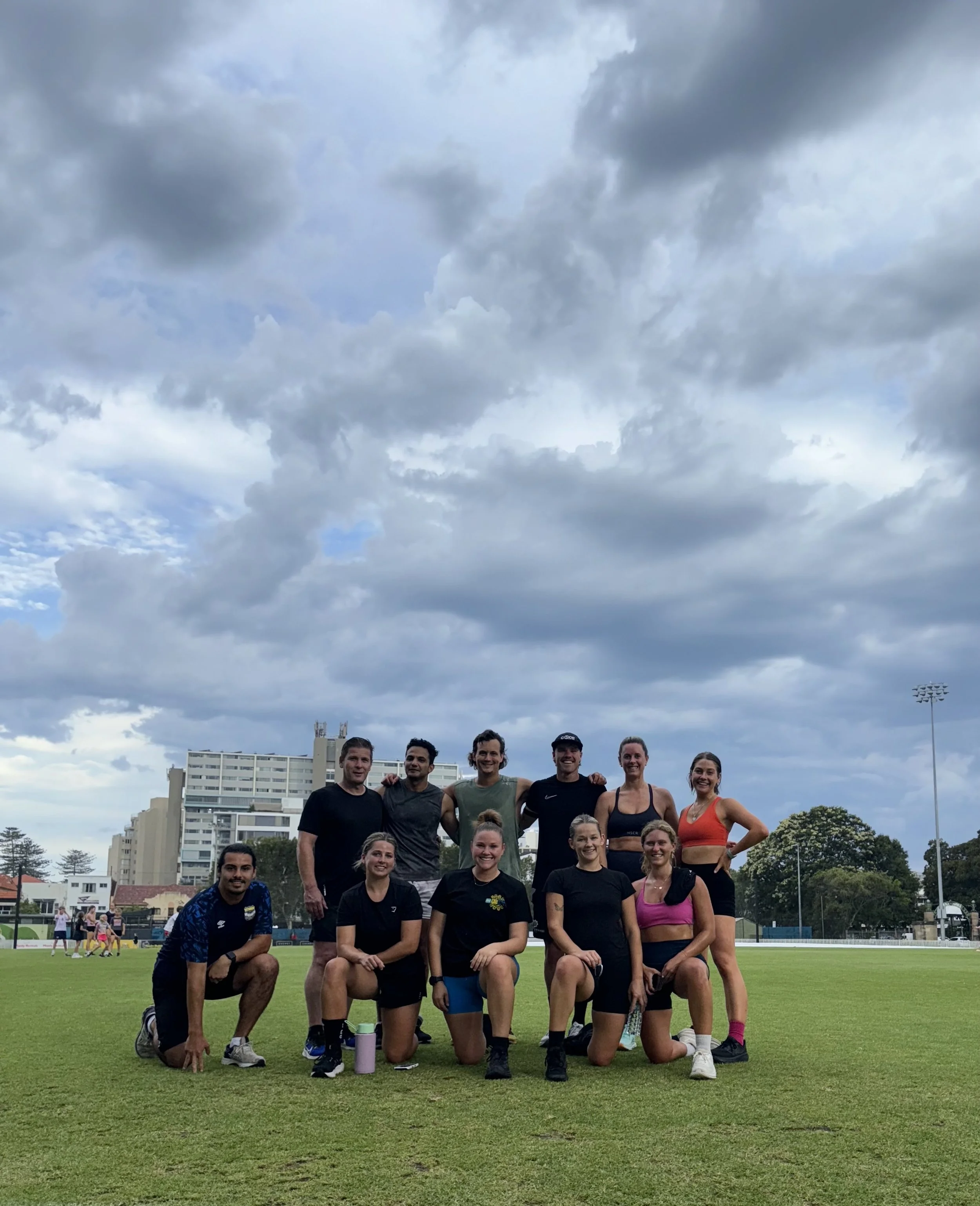Group of ten athletes on a track field under cloudy sky, posing for a team photo, some kneeling and some standing.