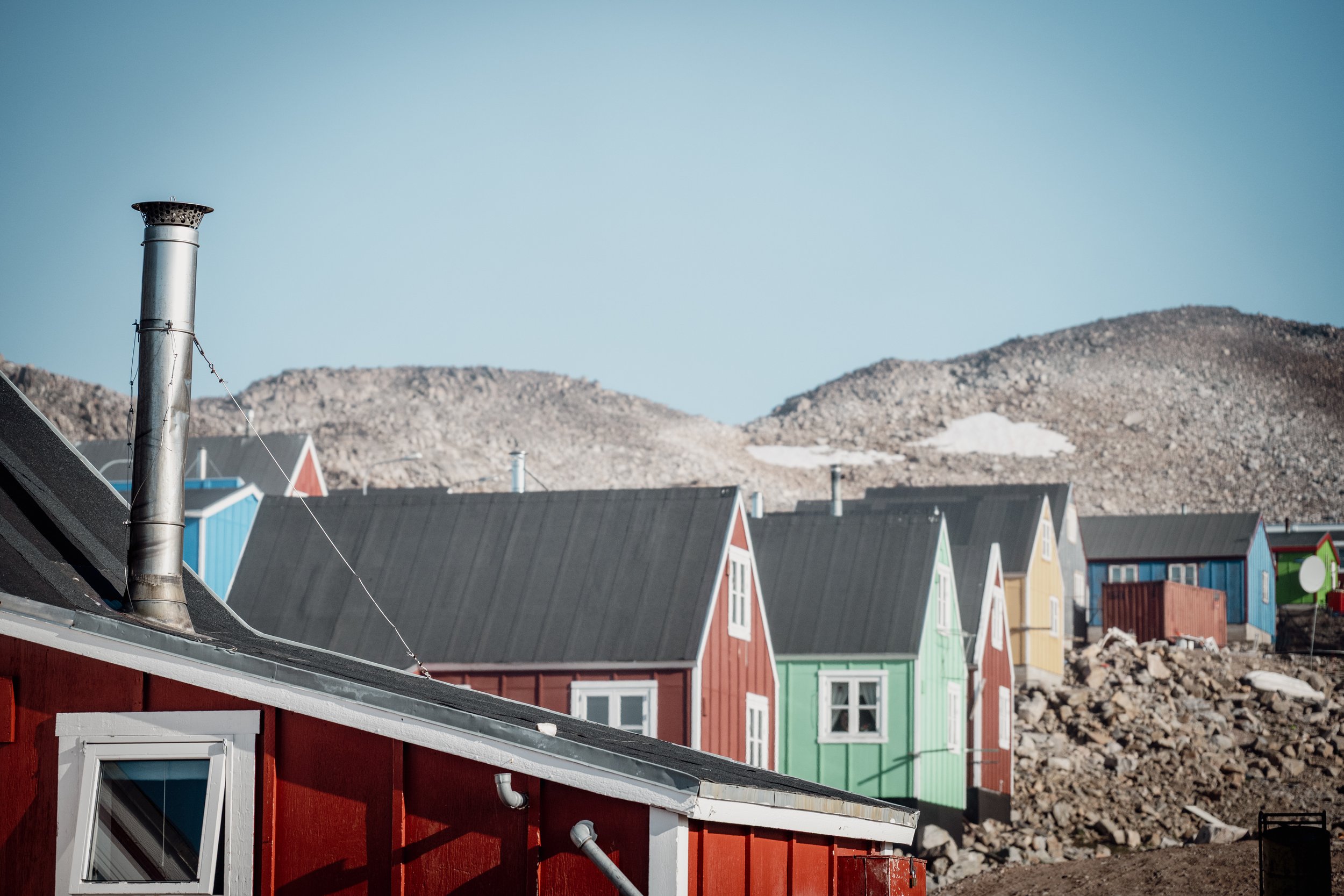 Colorful houses with pitched roofs and chimneys against a rocky landscape and clear sky.