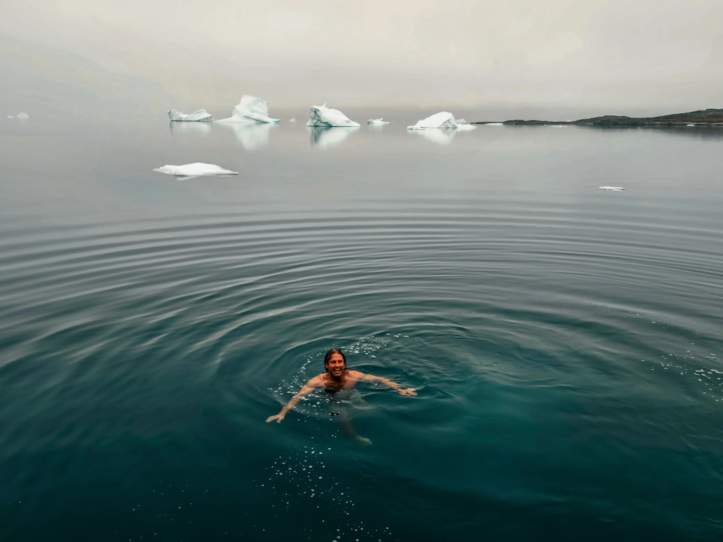 Person swimming in cold water with icebergs in the background