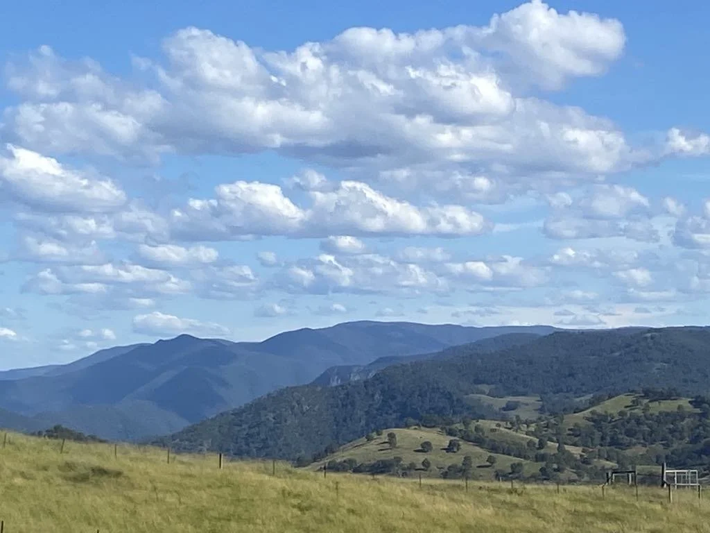 Scenic landscape of rolling green hills and mountains under a partly cloudy blue sky.