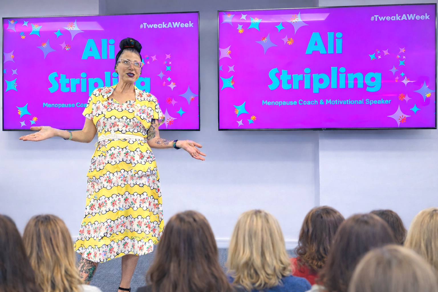 Ali Stripling is delivering an in-person session to women on menopause.  Ali is wearing a vibrant yellow dress and talking to a group of women.