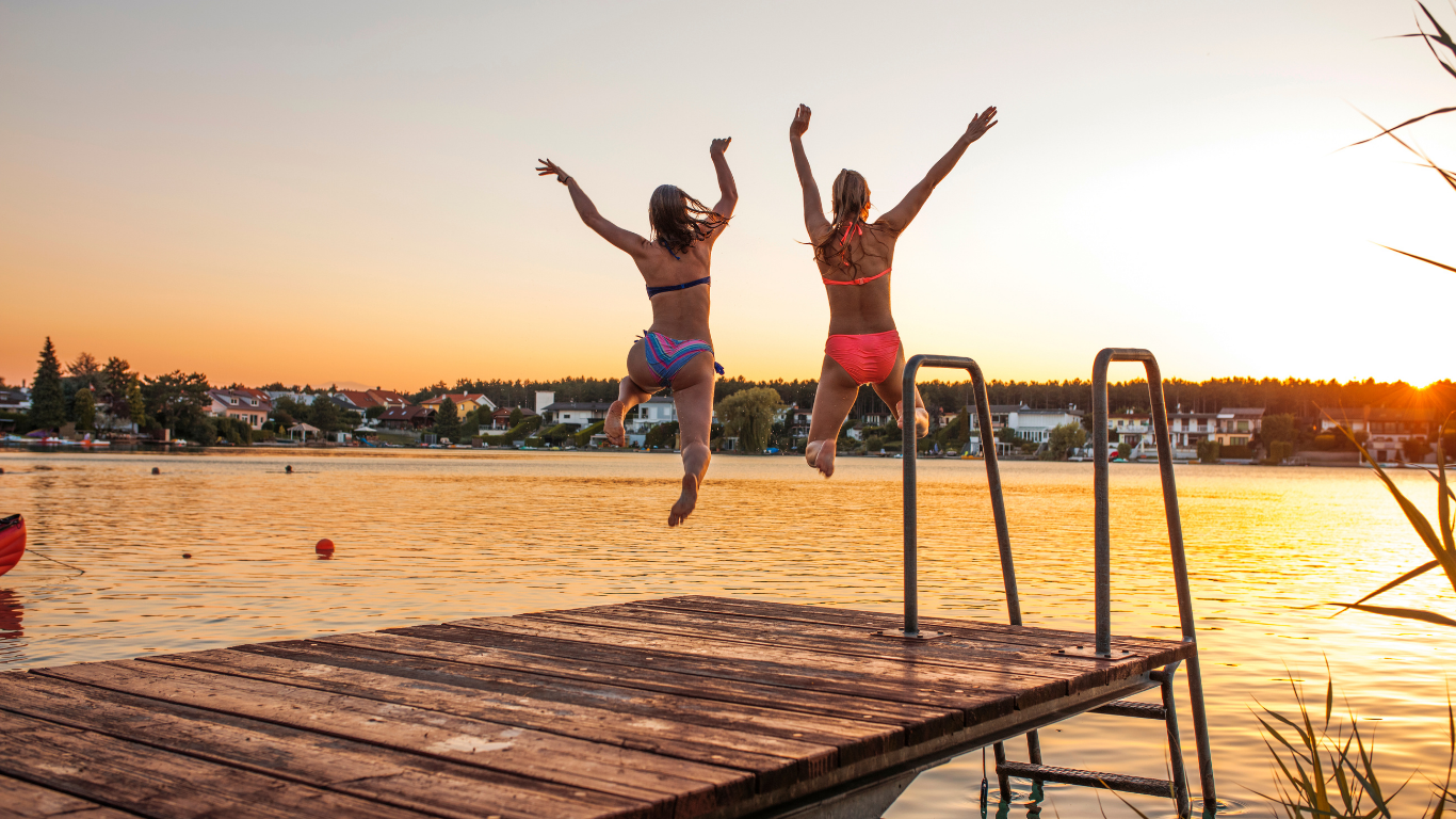 Two people jumping off a dock into a lake at sunset.