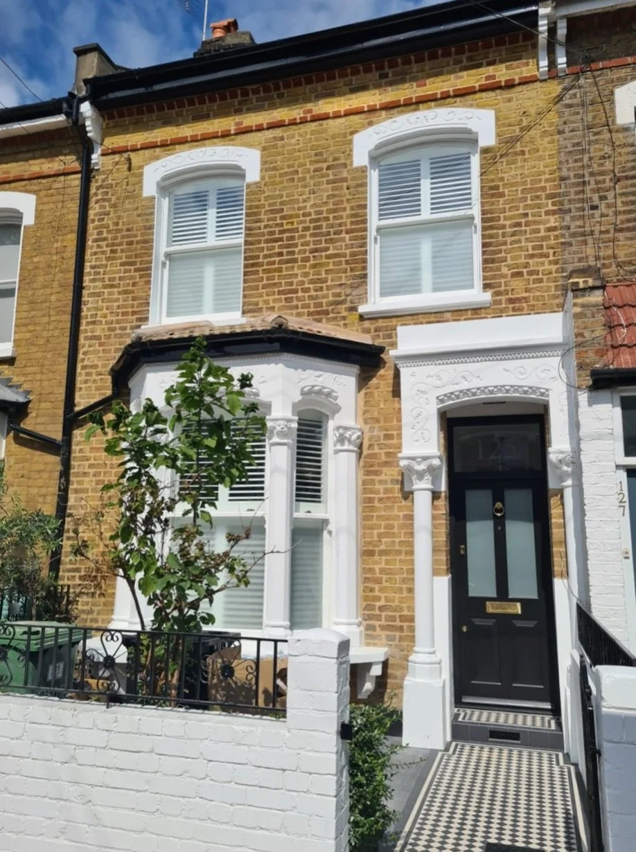 Victorian-style brick townhouse with bay windows and black front door, surrounded by white decorative moldings.