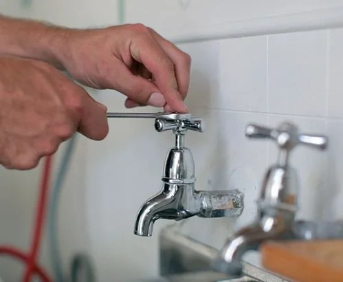 Person using a screwdriver to adjust a metal faucet in a bathroom or kitchen.