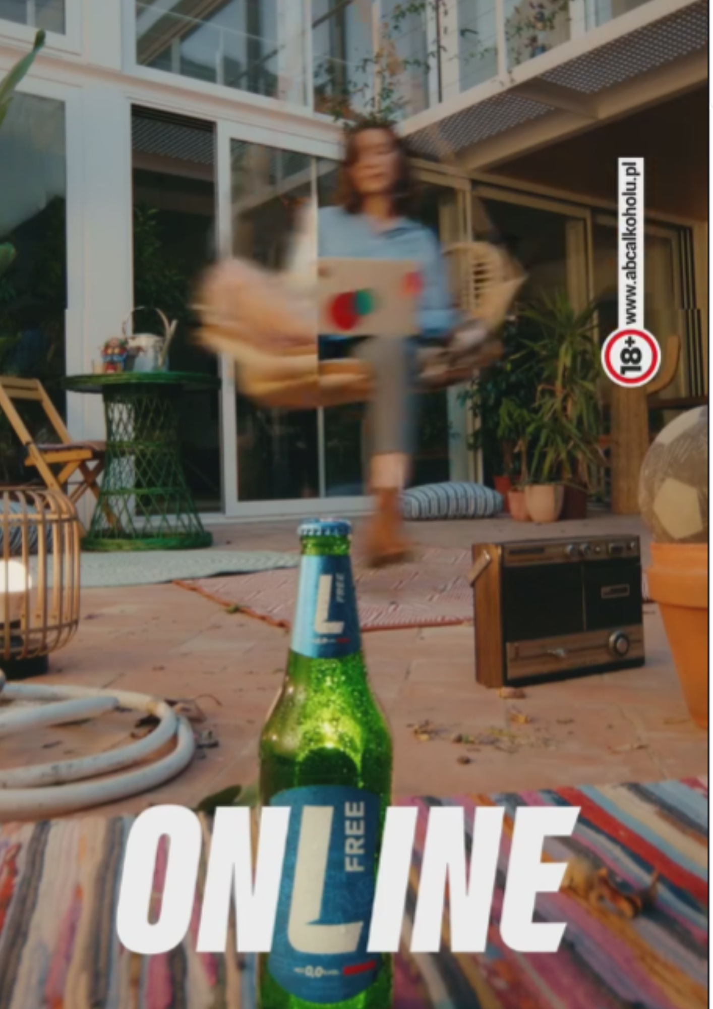 A person in a blue shirt is holding a tray with a drink, walking on a wooden patio with various outdoor furniture and plants, with a green glass bottle in the foreground and the word 'ONLINE' overlaid.