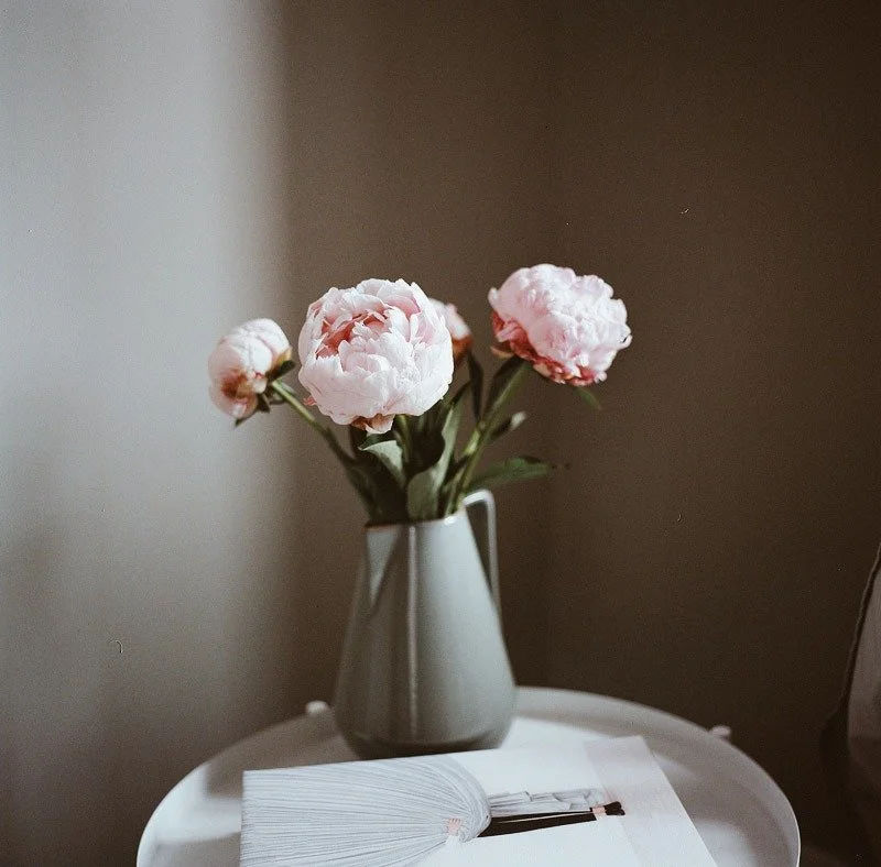 Gerbera i en vit vas på ett bord med en öppen bok framför.