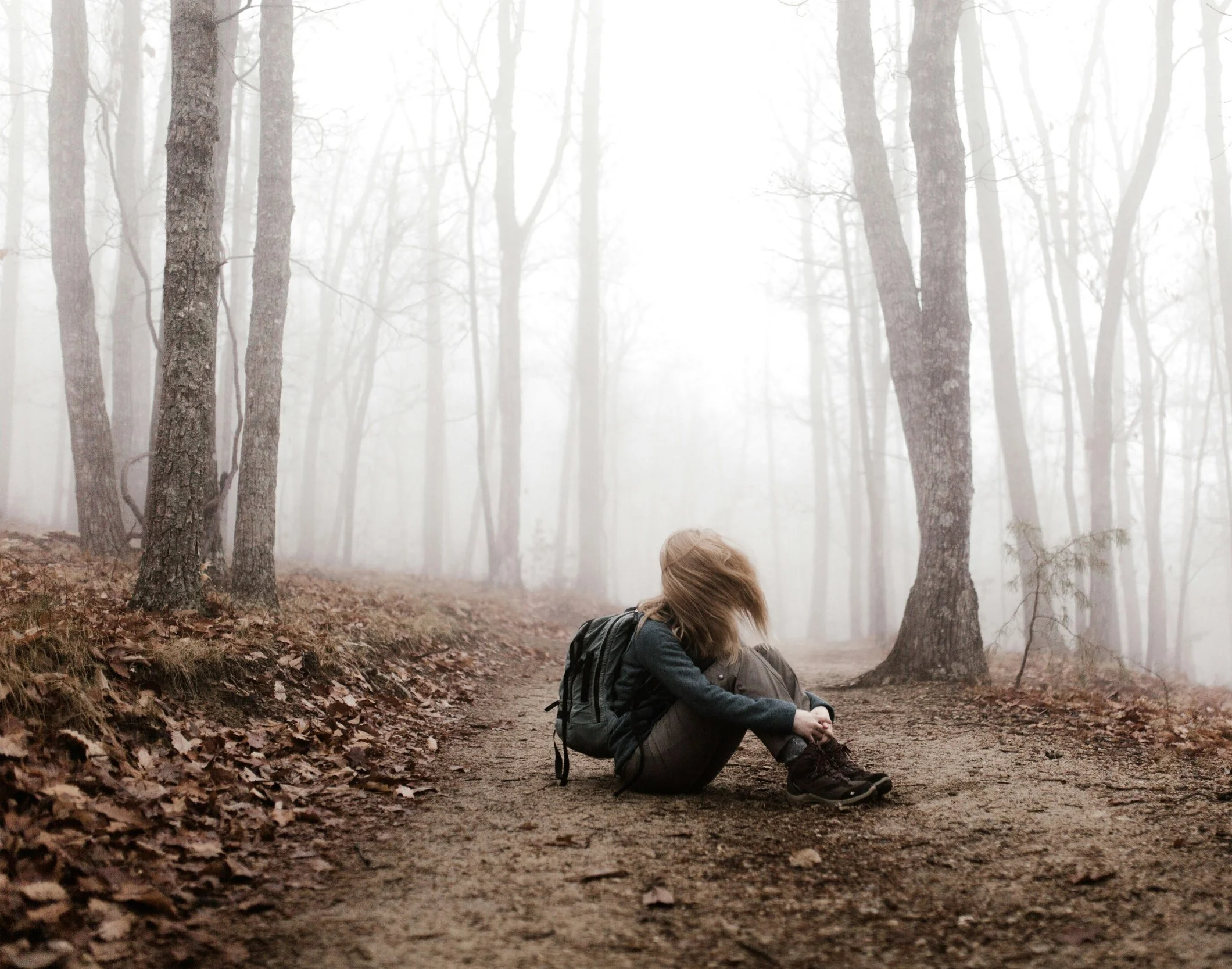 En person som sitter på en stig i en dimmig skog, med ryggsäcke.
