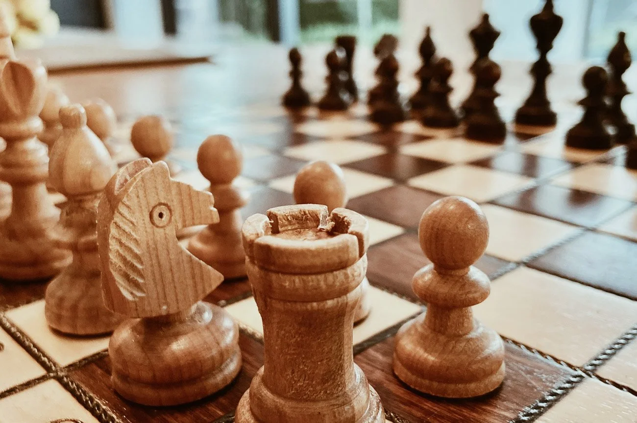 En schackbräda med träfigurer av schackpjäser i främre plan, inklusive en bonde och en springare.