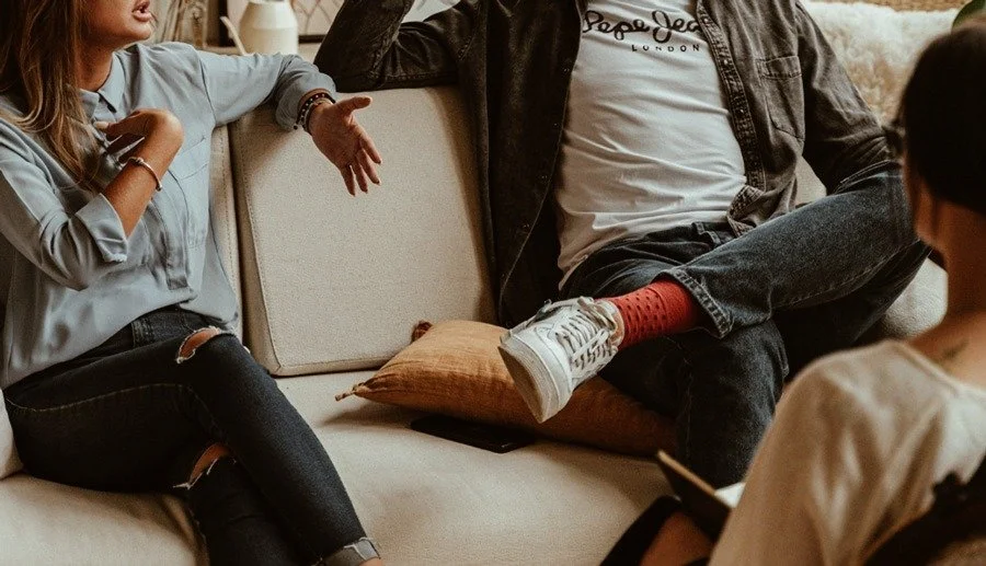 Tre personer som pratar i ett vardagsrum, sittandes på en soffa.