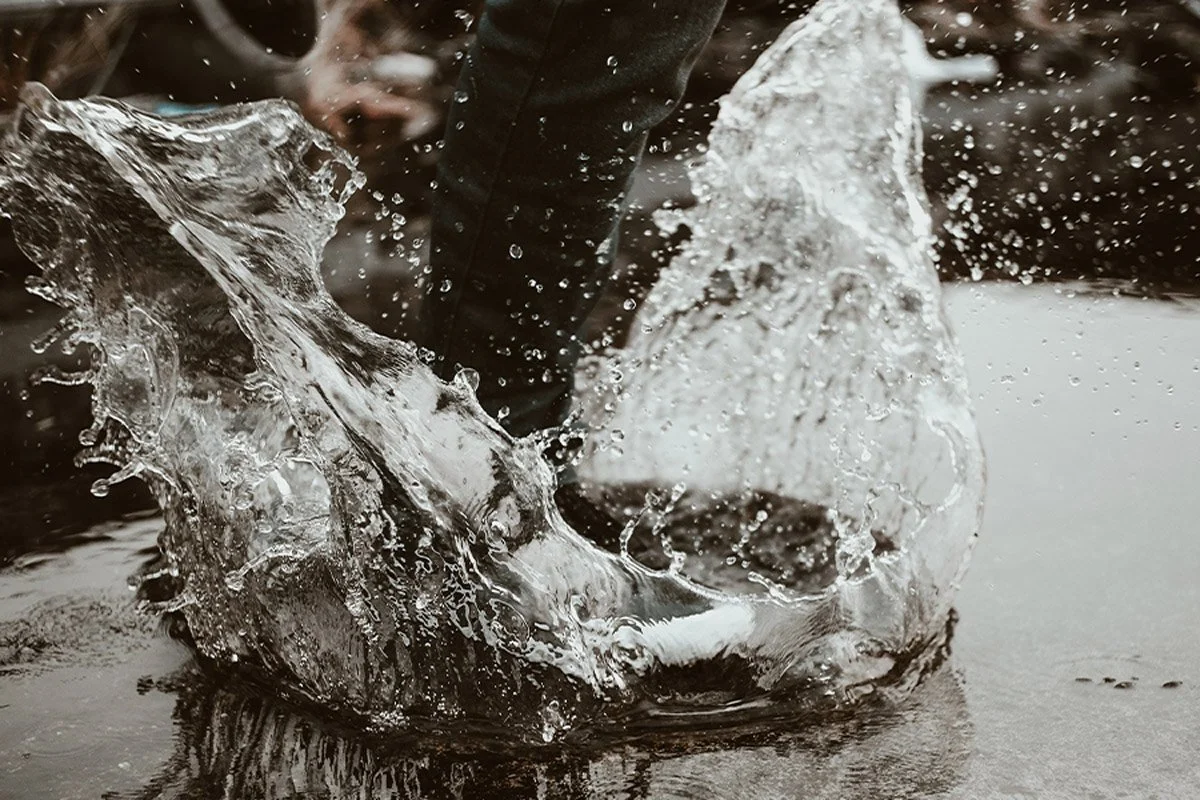 En närbild av en fot som träder ner i vatten, vilket skapar en våg och droppar.