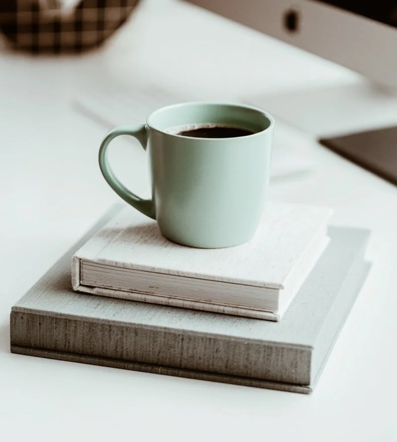 En kopp kaffe placerad på två böcker på ett vitt bord.
