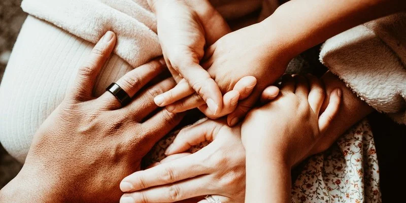 Flera händer som vilar tillsammans i en cirkel, symboliserar samhörighet och stöd.