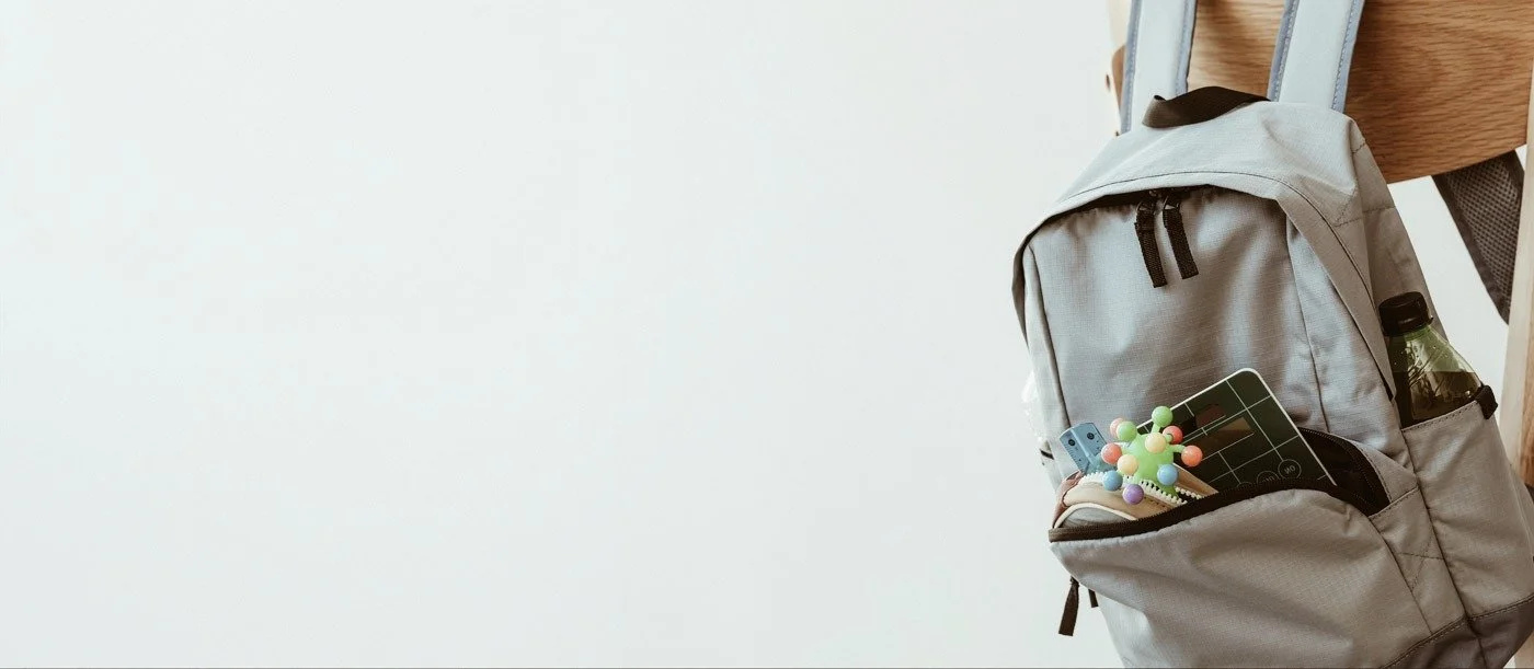 En grå ryggsäck hänger på en stol med några små leksaker och ett plåtskylt i ena lådan.