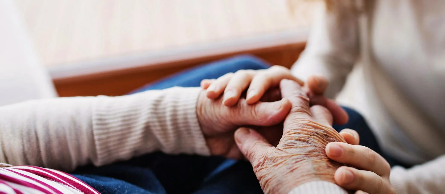 Närbild av en person som håller en äldre persons hand.