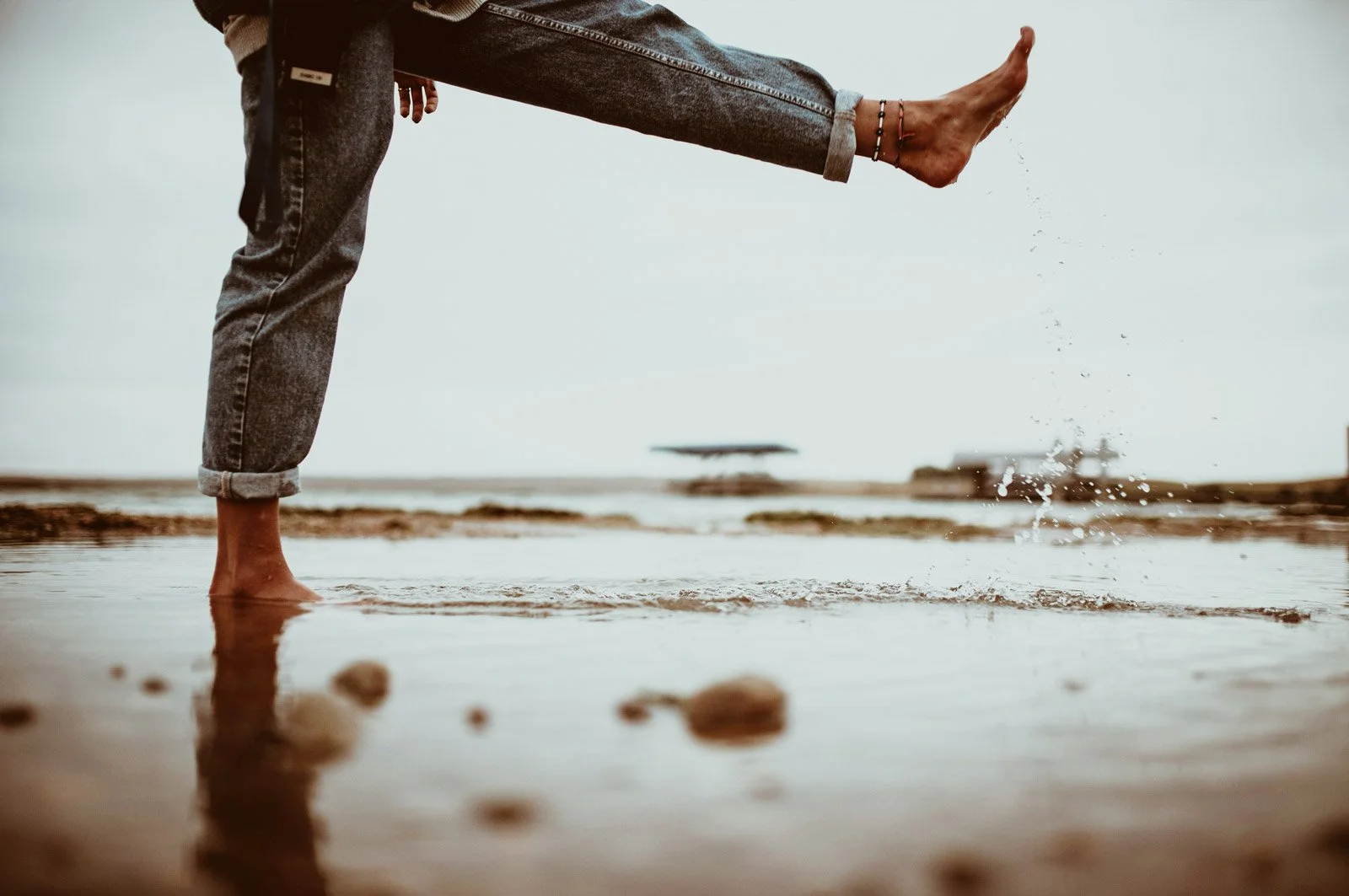 Personer står i vattnet på stranden, med en av personens ben i luften och vattnet som stänker.