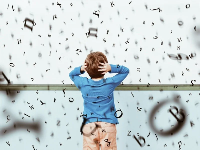 En pojke står med ryggen mot kameran, omgiven av flygande bokstäver och siffror, verkar förvirrad eller stressad.