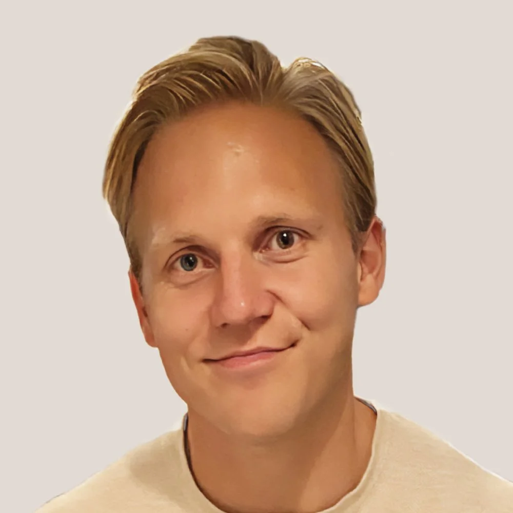 En kvinna med axellångt blont hår, glasögon och svart topp, ler mot kameran.