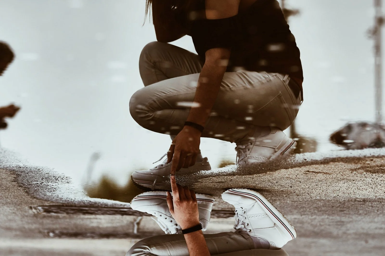 Två personer, en man och en kvinna, crounar vid en vattenpöl ute på gatan, där de pekar på något.