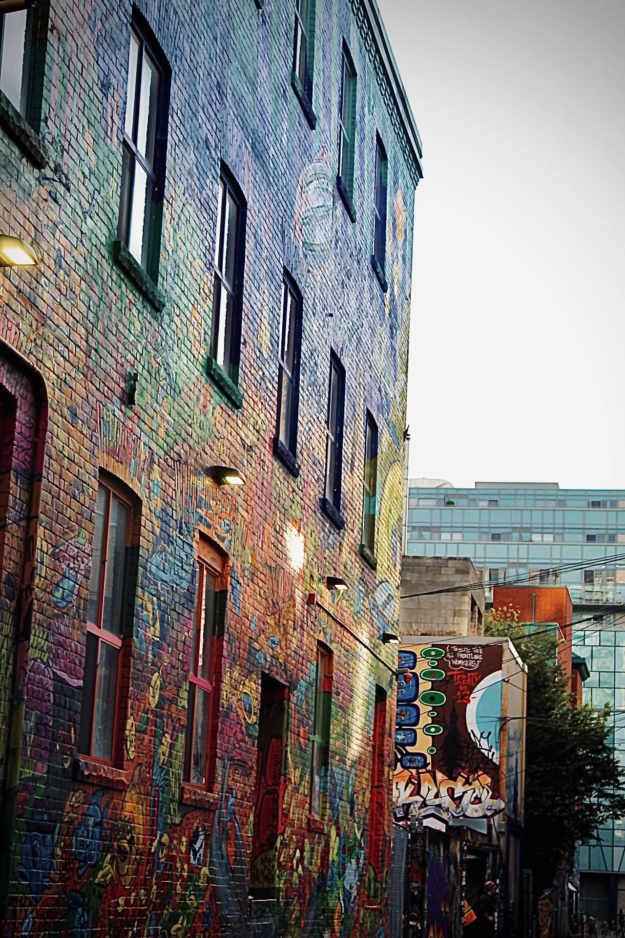 Colorful urban mural on a brick wall with windows and street art in an alley, surrounded by modern buildings.