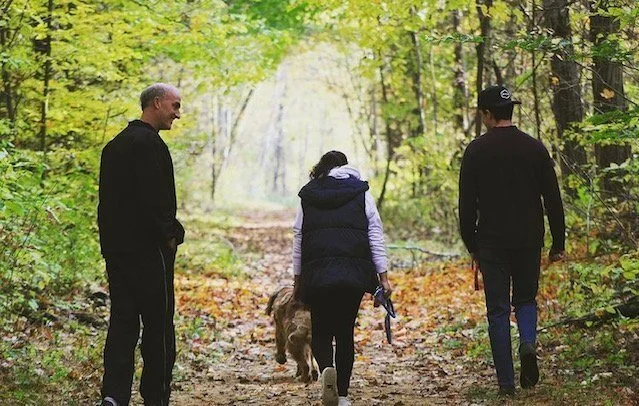 Three people walking a dog on a forest path in autumn.