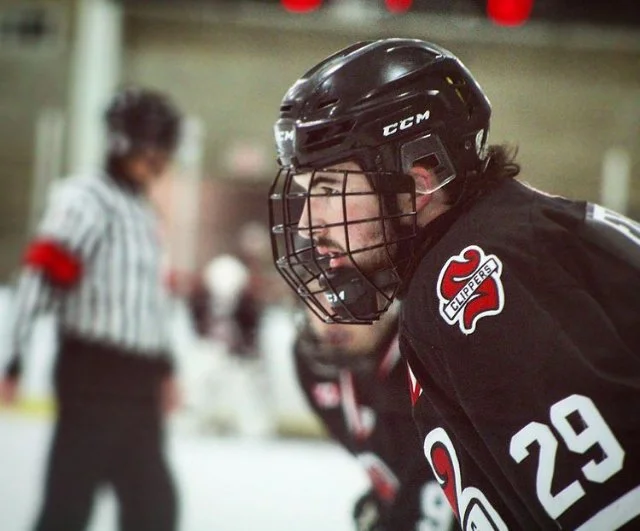 Hockey player wearing black helmet and jersey number 29, with "Clippers" logo on shoulder, during a game with referee in the background.