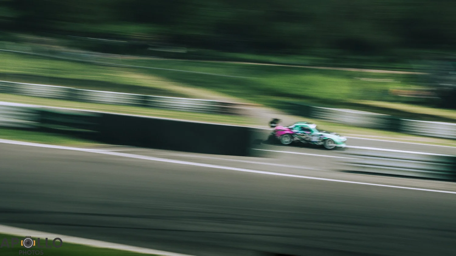 Turquoise and pink racing car captured with motion blur at Cadwell Park.