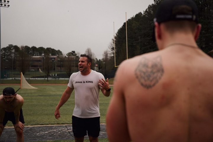 Group of people exercising outdoors on a sports field, focusing on a man wearing a "Jesus is KING" t-shirt.