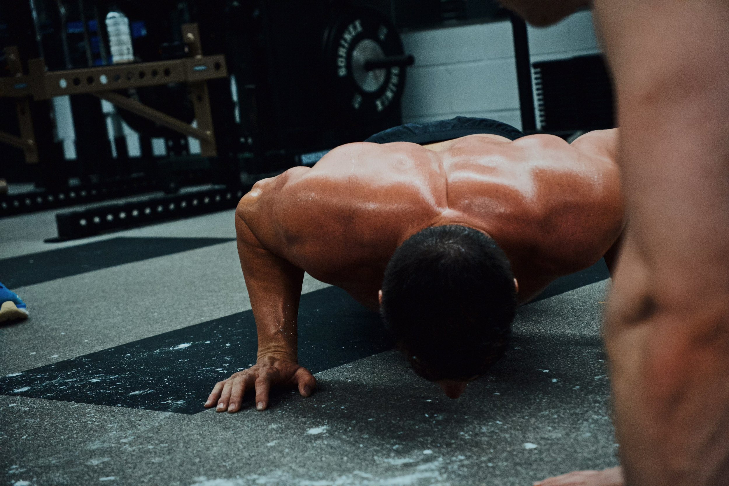 Man doing push-ups in a gym with weights in the background.