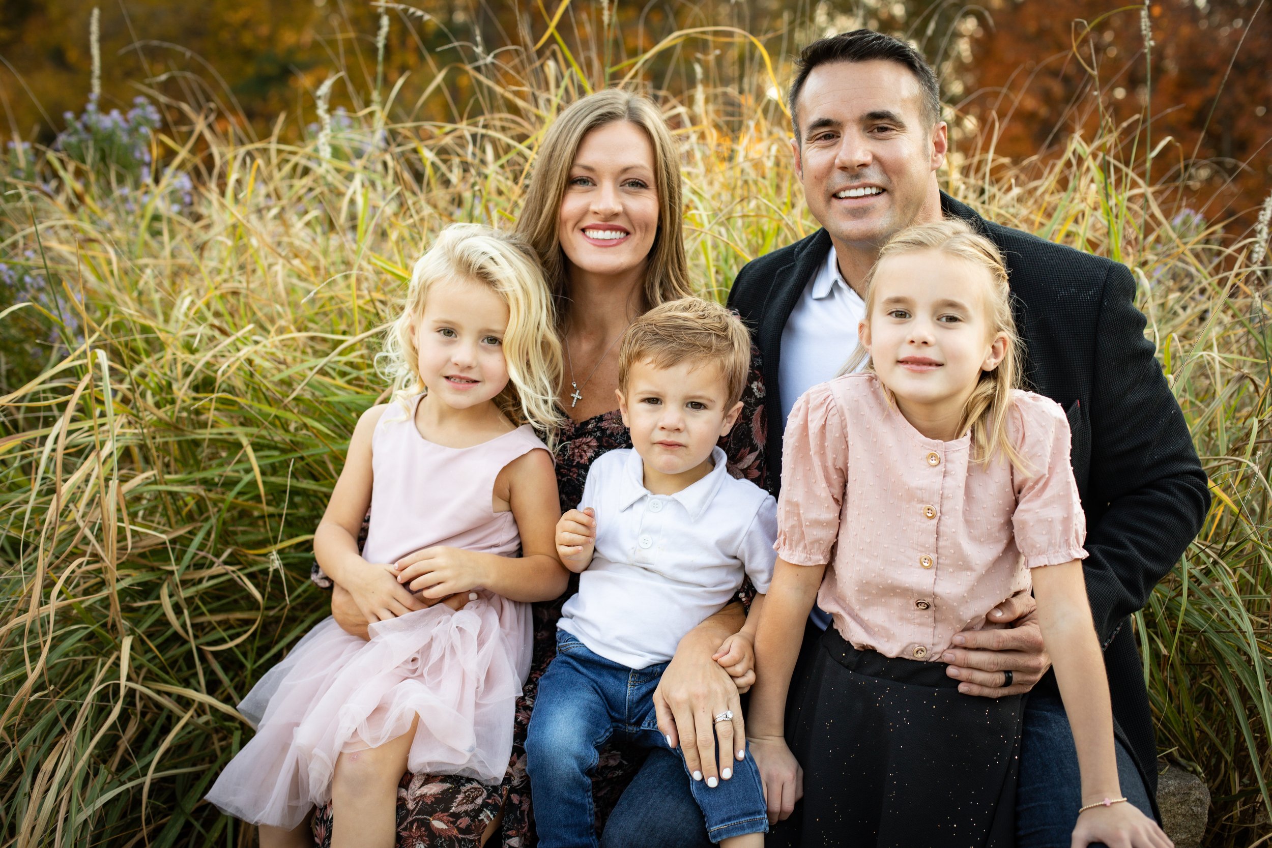 Happy family with three children sitting outdoors in autumn setting.