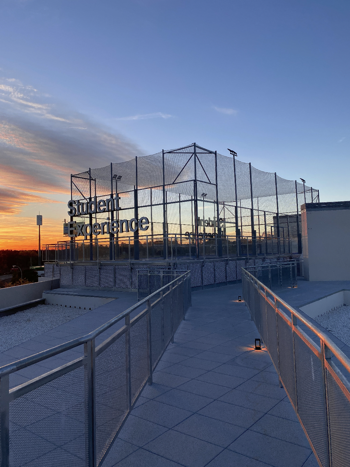 Rooftop sports court at sunset with the words 'Student Experience' on the metal fence.