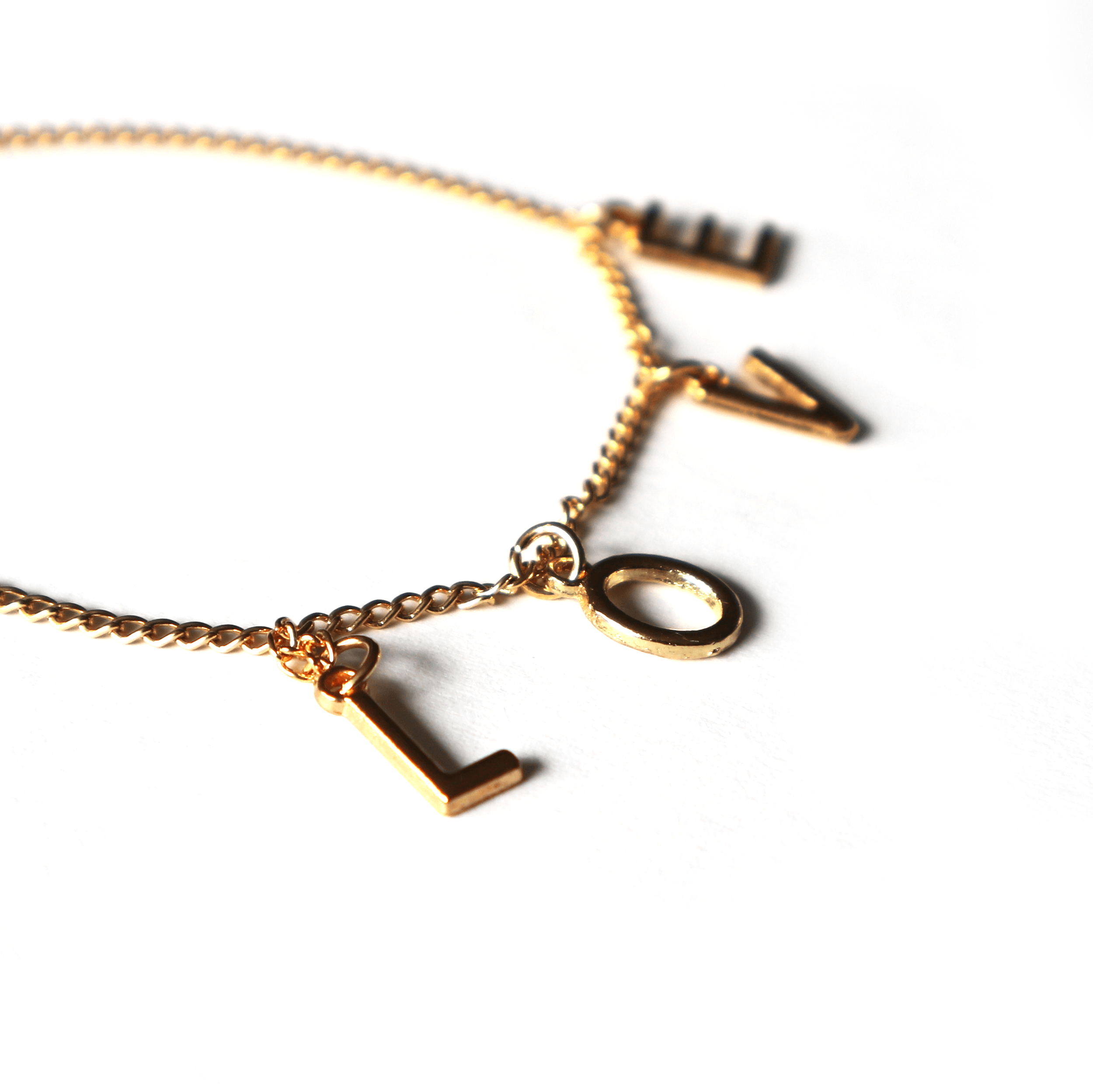 Close-up of a gold necklace with the word "LOVE" spelled out in individual gold letter charms on a white surface.