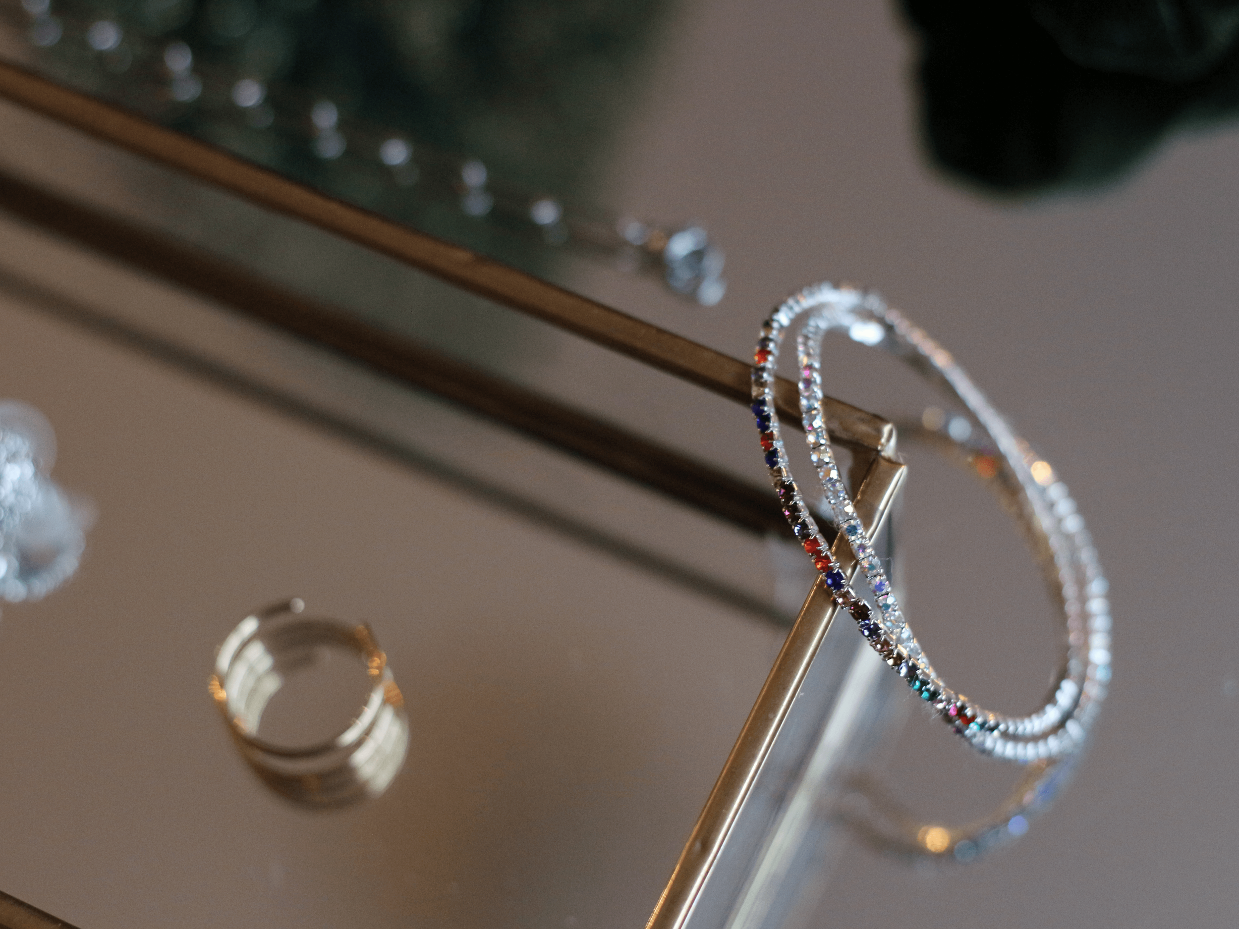 Silver and colorful gemstone bracelets and rings displayed on a glass jewelry stand.